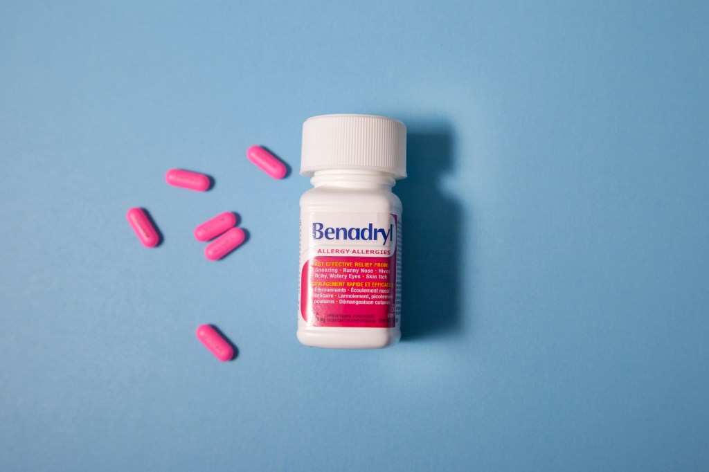 Bottle of Benadryl allergy medicine with scattered pink pills on a blue background.