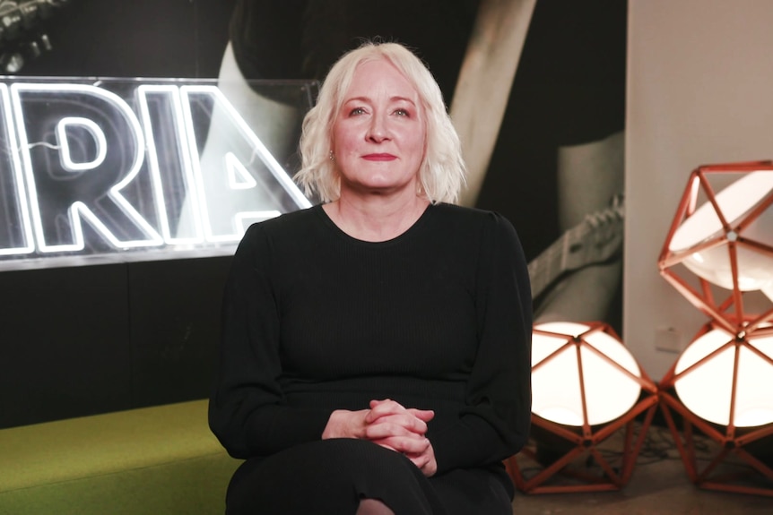A woman in black sits in front of an ARIA sign. 