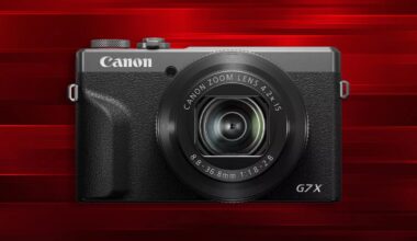 A Canon G7X digital camera with a zoom lens is displayed against a red, striped background.