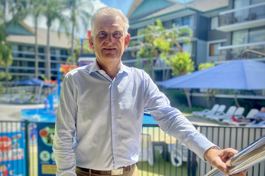 A man in a white business shirt standing with his arm on a pole.