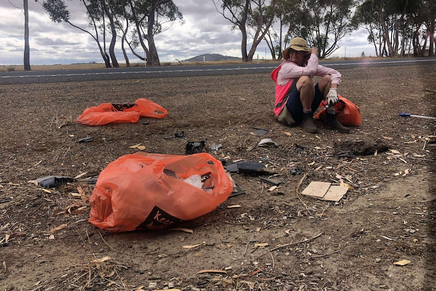 A woman sits on the side of the road surrounded by rubbish