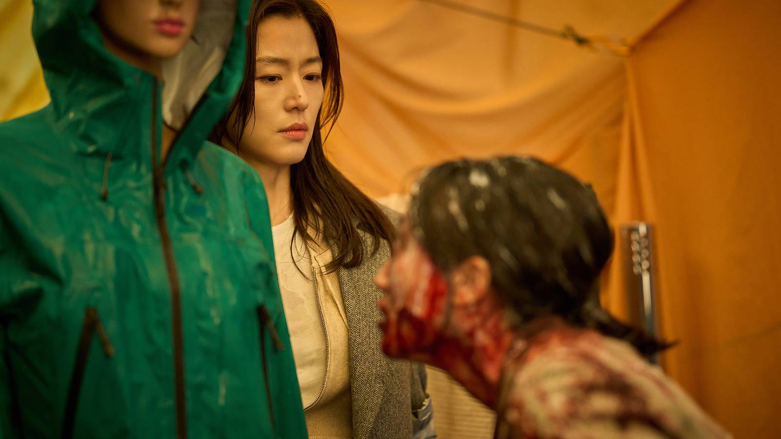 A frightened-looking Korean woman tries to keep emotion off her face while a blood-covered humanoid sniffs at her in Colony