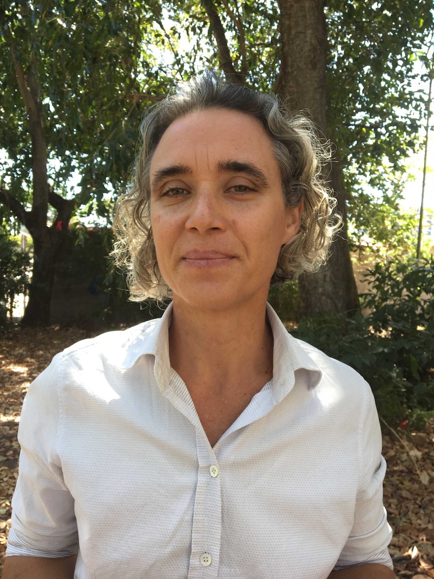 Adele poses for portrait under a tree with mottled light striking her light patterned shirt with open collar.