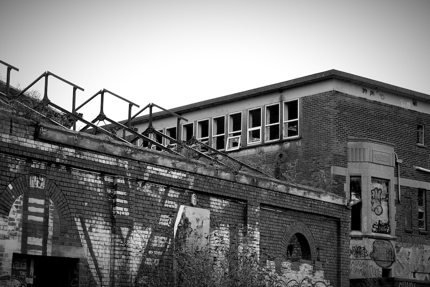 A brick building without a roof and beams exposed, smashed windows.
