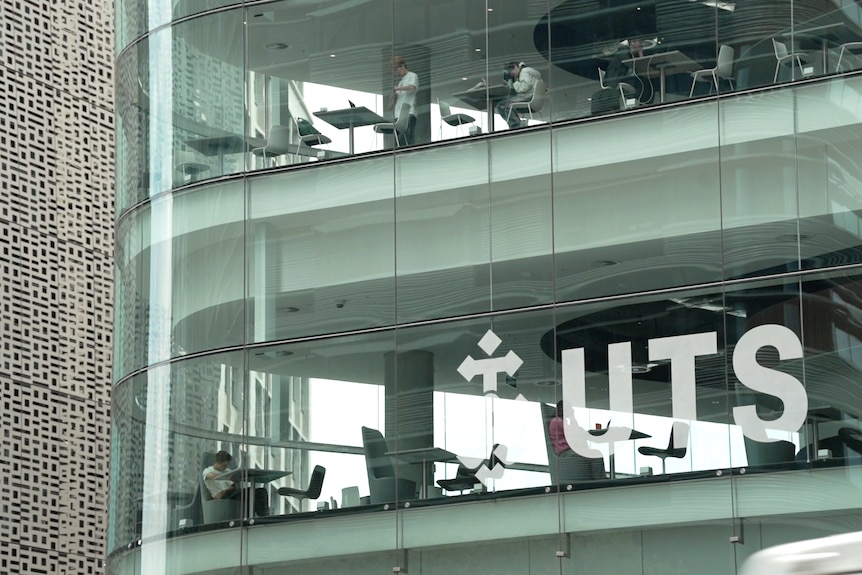 Tables can be seen inside two floors of a glass building with "UTS" on the side of it.