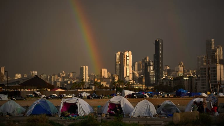 Displaced people who fled Israeli strikes in southern Lebanon sit inside tents used as shelters as a rainbow breaks through the rain in Beirut, Lebanon, Sunday, March 29, 2026.