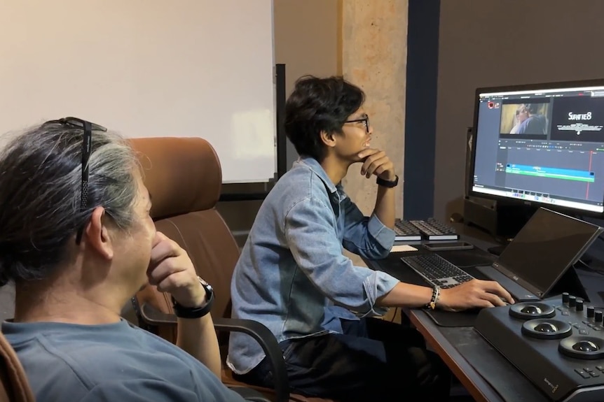 Two men sitting down in front of computer screens.