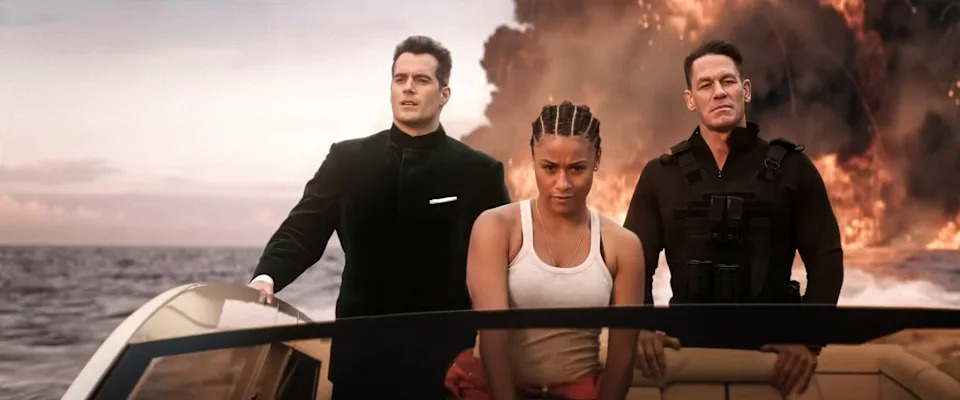 Three people on a speedboat, dressed in action movie attire, with a fiery explosion in the background