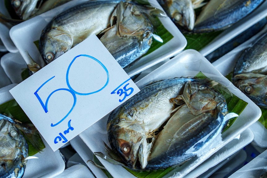 A row of trays containing two fish and a banana leaf each, with a price tag of 50.35 baht written in blue marker pen.
