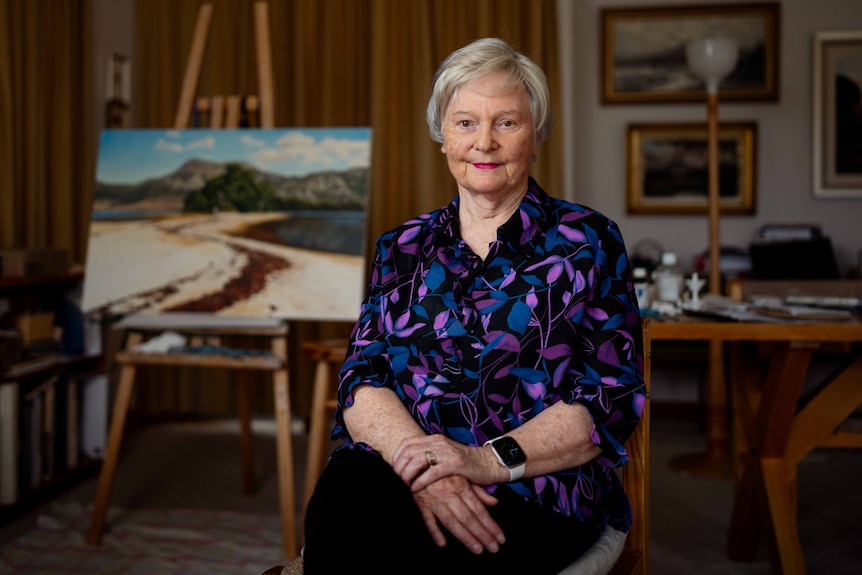 Woman smiles for photo, sitting in front of a painting.