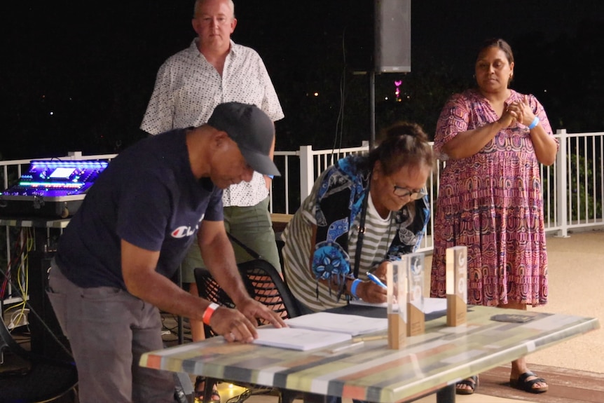 man and woman lean to sign stacks of papers on table