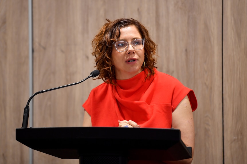 Amanda Rishworth speaks at a podium in a red dress.