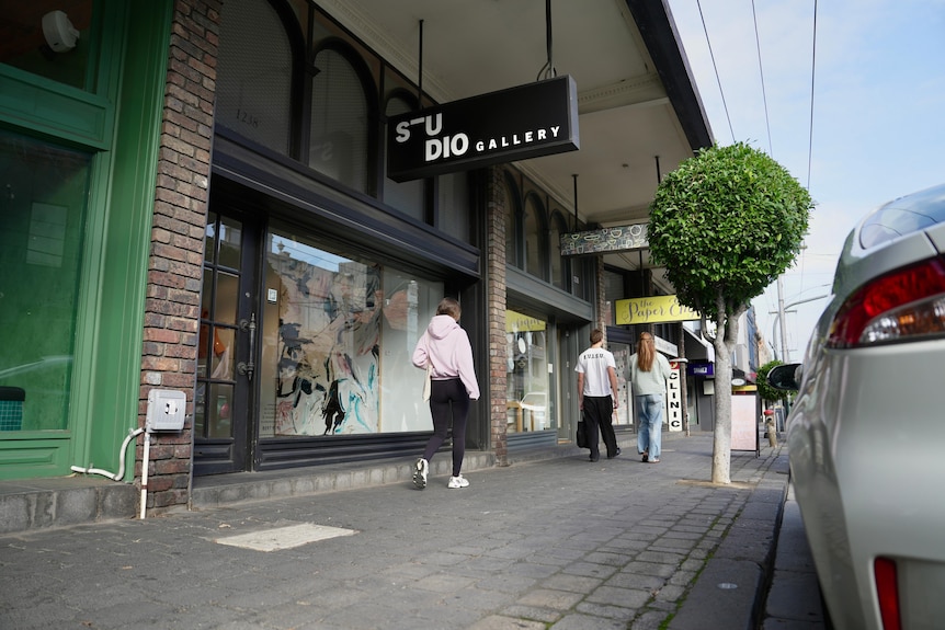 A woman in a pink shirt walks past a shop with a big glass window on a Melbourne street. The shop sign says Studio Gallery