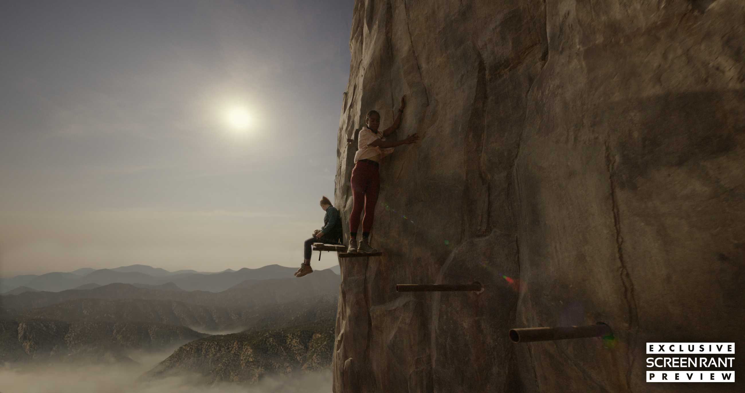 Two people walking on planks on the side of a mountain in Fall 2