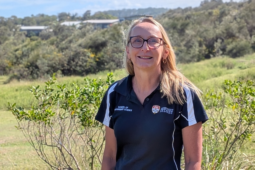 Woman in University of Sydney shirt in coastal landscape with houses behind