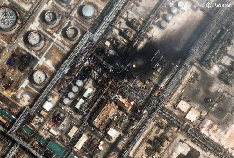 An overhead view shows a heavily developed industrial area with burned buildings and smoke rising.
