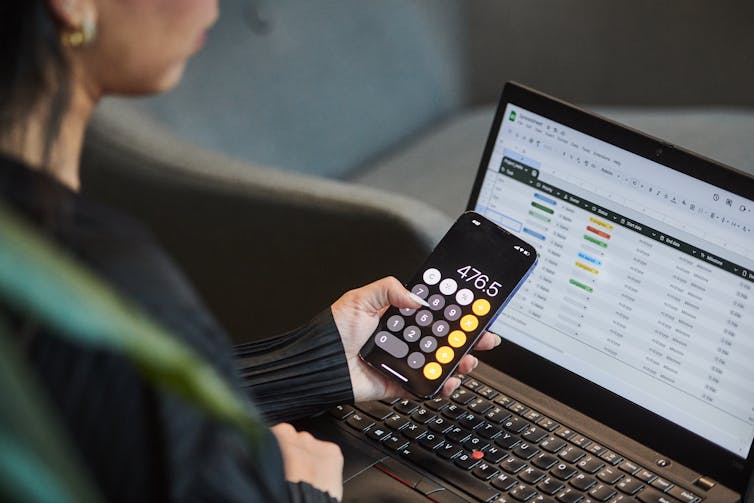 A person uses the calculator app on their phone while working on a spreadsheet
