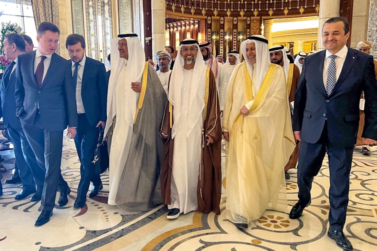Men in suits and traditional Gulf attire stand.