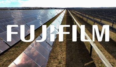 Rows of solar panels in a large field under a bright sky, with the word "FUJIFILM" in bold white letters overlaid across the center of the image.