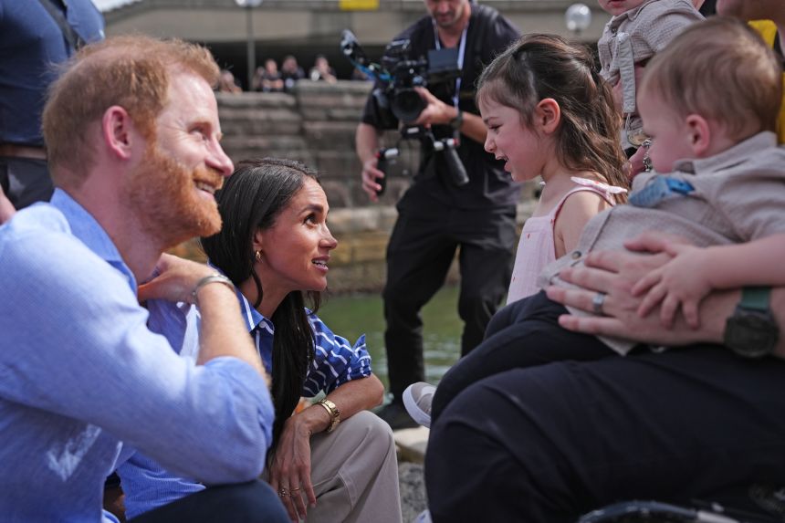 Prince Harry and Meghan talk to Charlotte, daughter of veteran Joel Vanderzwan at a sailing event with members of Invictus Australia in Sydney Harbour.