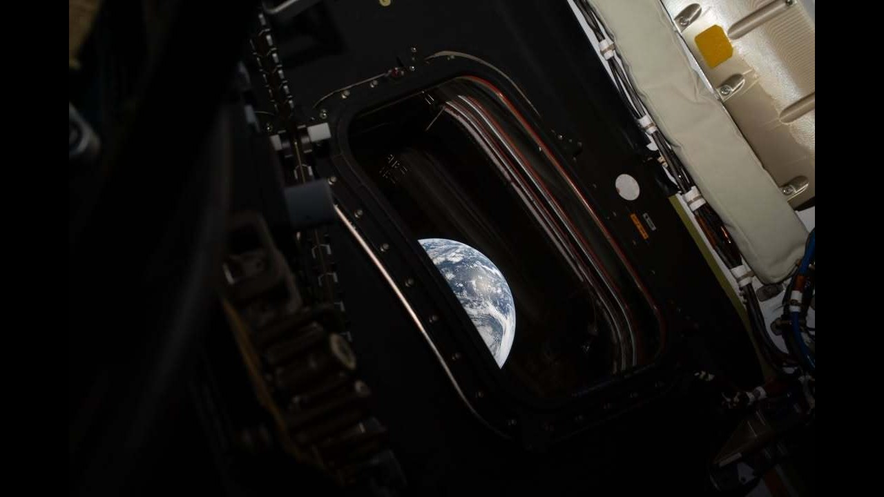 a photo of a blue and white planet as seen through a small window in a spacecraft cabin