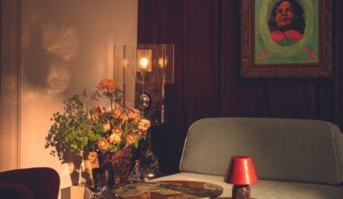 A sun-lit living room decorated with artisanal pieces in glass, wood, marbled copper, fresh flowers, plush, velvety seats, and a colorful artwork hanging on the wall.