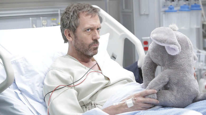 Hugh Laurie as Dr. Gregory House lying in a hospital bed holding a stuffed elephant in House