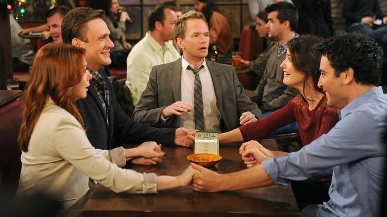 Lily, Marshall, Barney, Robin, and Ted holding hands at a bar in How I Met Your Mother