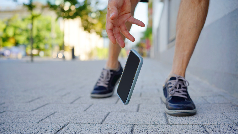 person trying to catch smartphone in a case as it falls toward the concrete ground outside.