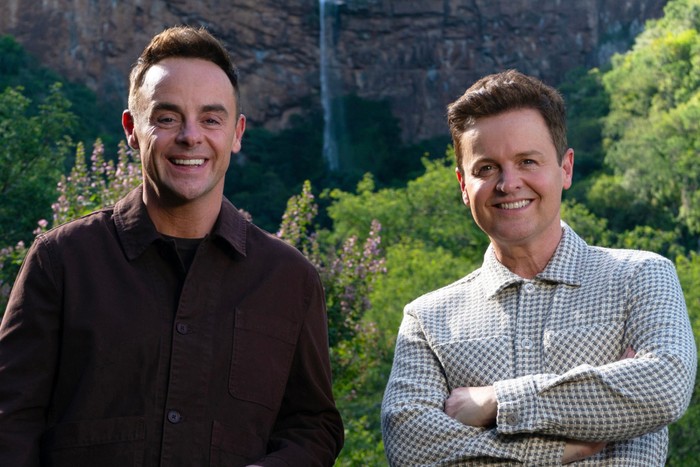 im-a-celebrity Ant and Dec stood next to each other with a forest backdrop, smiling ahead.