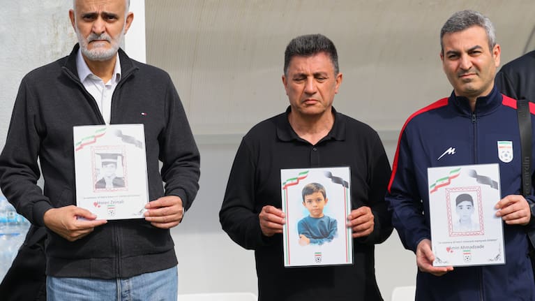 Iran's coach Amir Ghalenoei, center, and Iran's Football Federation Vice President Mehdi Mohammad Nabi, left, hold pictures of children allegedly killed in a US and Israel strikes.