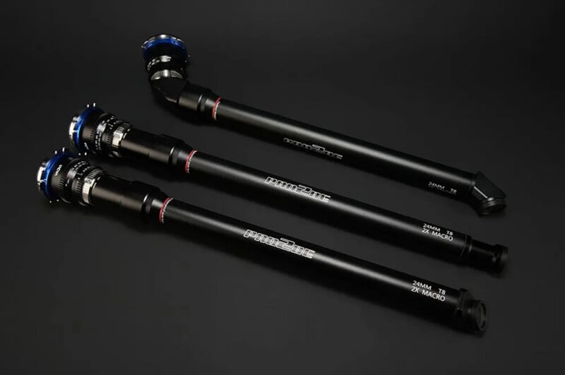 Three black probe camera lenses with blue accents are displayed on a black surface, arranged diagonally and labeled "24MM T8 2X MACRO PROBE" and "LAOWA.