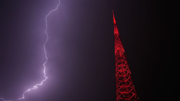 Lightning lights up the sky behind a television tower as a thunderstorm moves through the area.