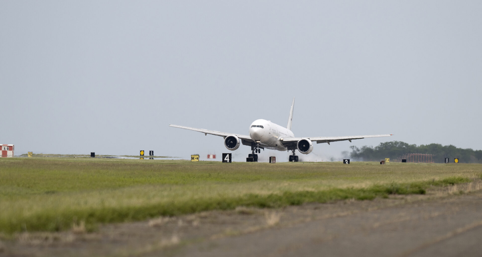The white 777 aircraft can be seen touching down on a long runway with a row of grass along the pavement at NASA's Langley Research Center.