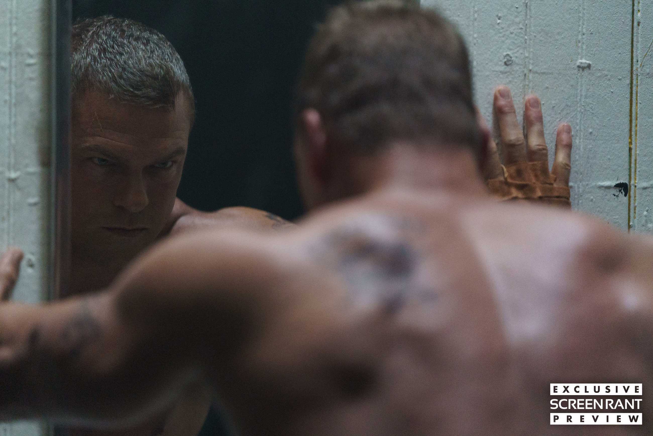 Alan Ritchson looking angry leaning up to a mirror in Motor City