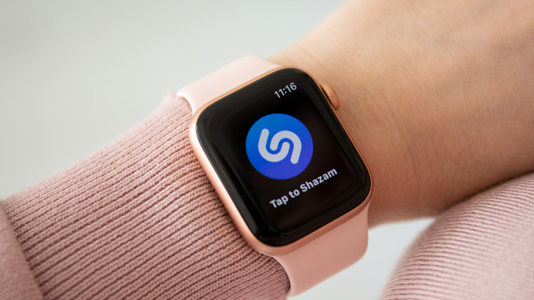 An Apple Watch with a pink band on a women's wrist displaying the Shazam logo