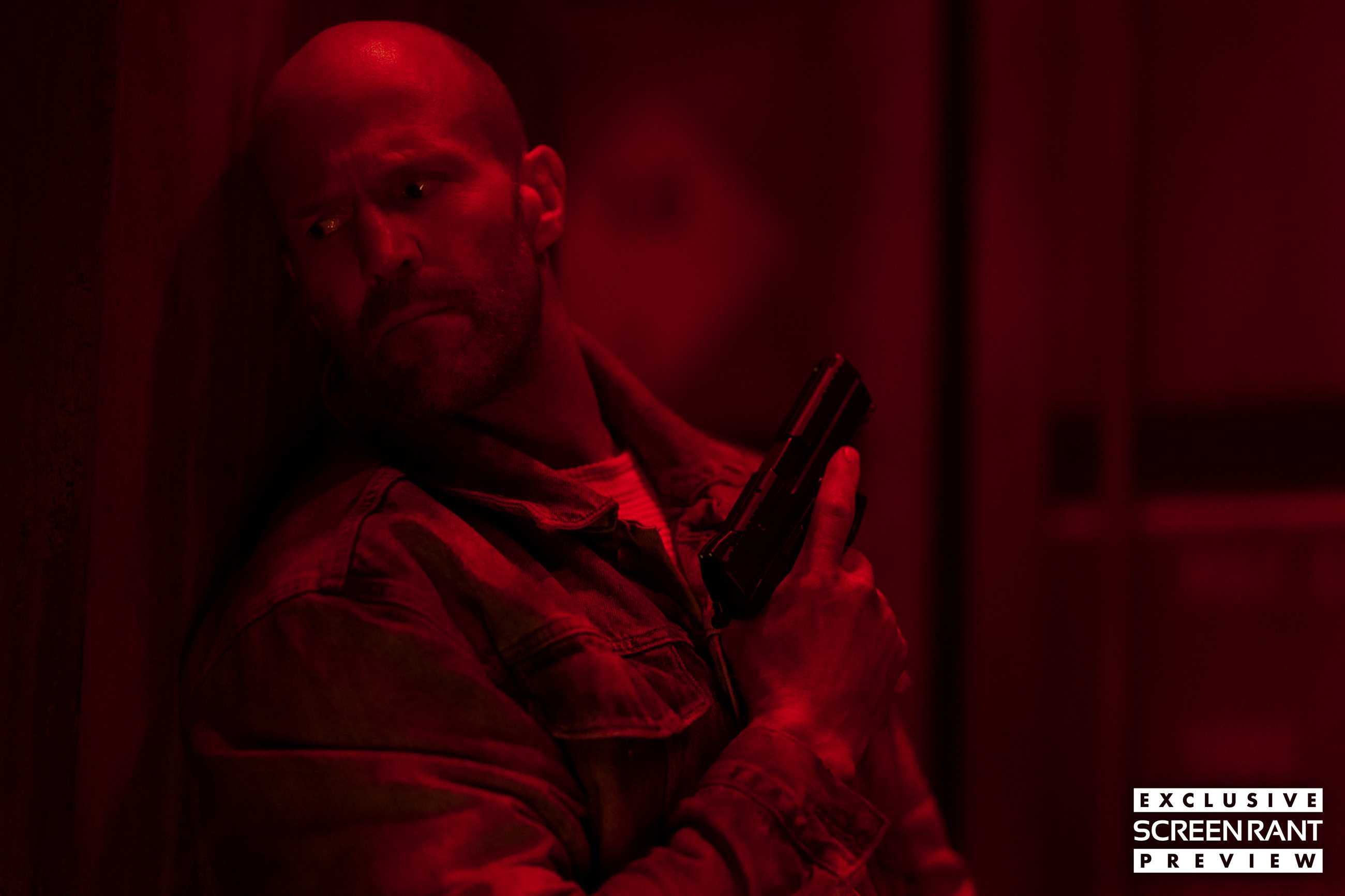 Jason Statham holding a gun and lit by red light in Mutiny