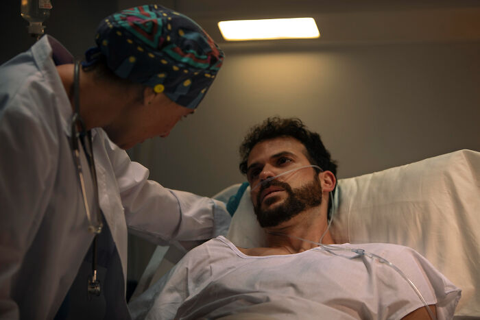 Surgical staff comforting a male patient in a hospital bed during sedation before surgery.