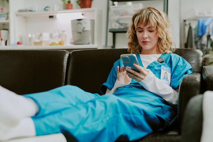 Surgical staff in scrubs on a couch, using a smartphone, reflecting on unhinged things patients confessed under sedation.