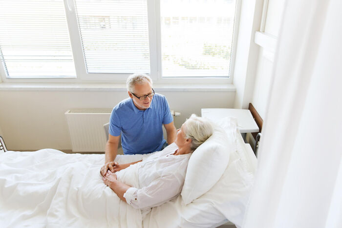 Elderly man comforting a patient in a hospital bed, representing surgical staff and patient interactions under sedation.