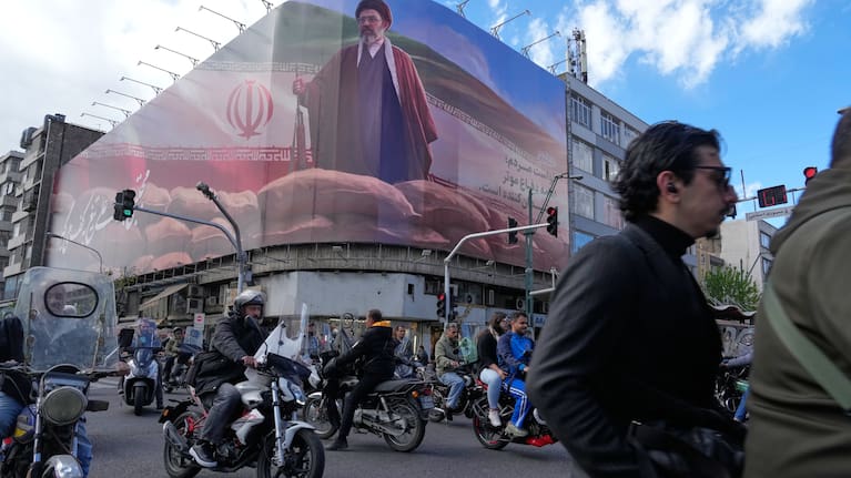 People drive their motorbikes past a billboard that shows a graphic depicting Iran's Supreme Leader Ayatollah Mojtaba Khamenei in downtown Tehran, Iran.