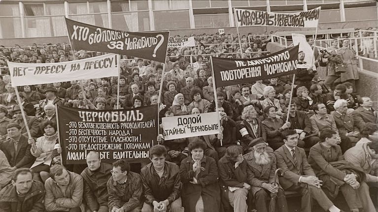 People hold signs reading "Down with the Chernobyl mysteries!" and "Who is responsible for Chernobyl?" during a protest rally demanding the truth about the Chernobyl nuclear power plant accident at a stadium in Chernobyl, Ukraine, April 26, 1989.