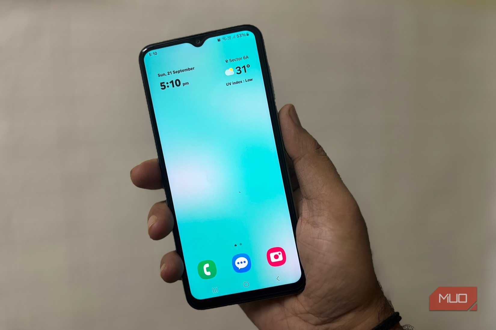 Person holding Samsung phone showing clean home screen with clock and weather