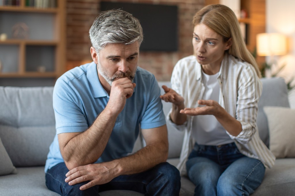 A woman yells at a man on a couch, who looks upset.