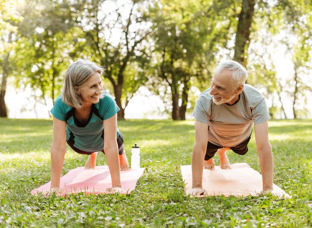 Senior couple, smiling, mature man and woman doing plank exercise together outdoors in park on yoga mat. Fitness, sport concept