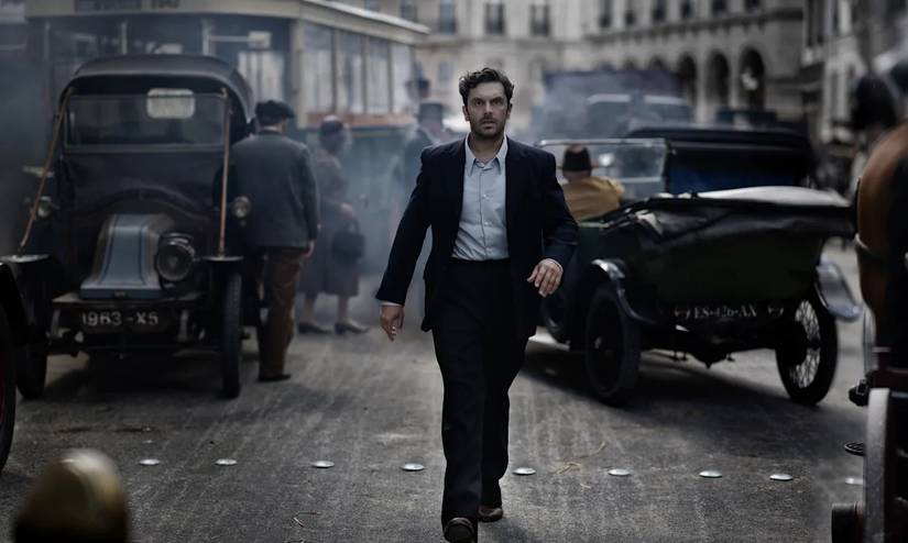 A man walking toward the viewer as cars drive around in the background