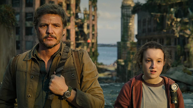 Joel standing next to Ellie in front of rundown buildings