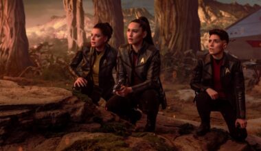 Enterprise crew members on an alien planet hunched down and surveying the terrain