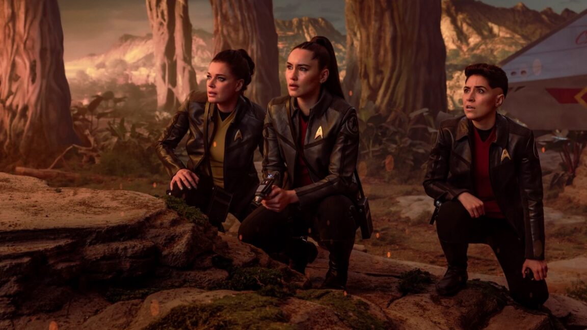 Enterprise crew members on an alien planet hunched down and surveying the terrain