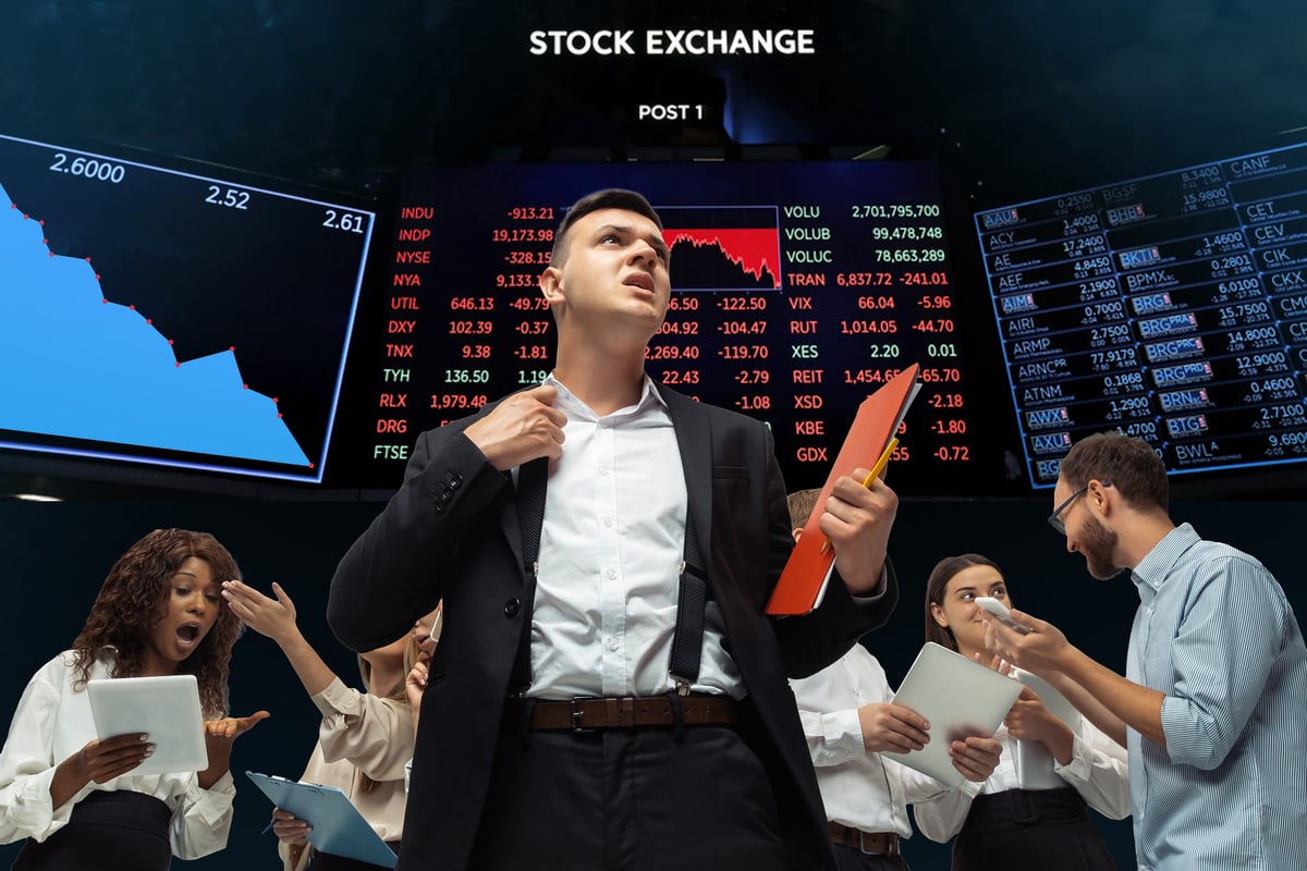 A stock trader holding a red folder looks worried on the floor of a stock exchange.